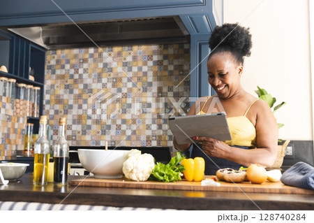 Mature African American woman standing at kitchen island, holding tablet with produce, copy space 128740284