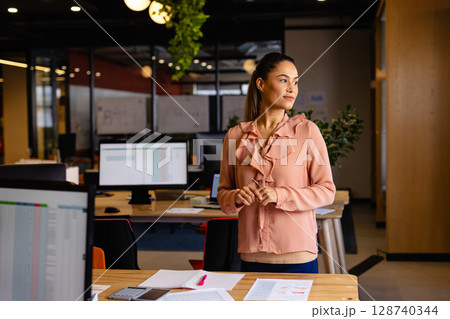 Businesswoman standing at wooden desk in office, using pink highlighter on papers, copy space Businesswoman standing at wooden desk in office, using pink highlighter on papers, copy space 128740344