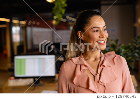 Professional woman smiling and looking in open-plan office with spreadsheet monitor, copy space Professional woman smiling and looking in open-plan office with spreadsheet monitor, copy space 128740345