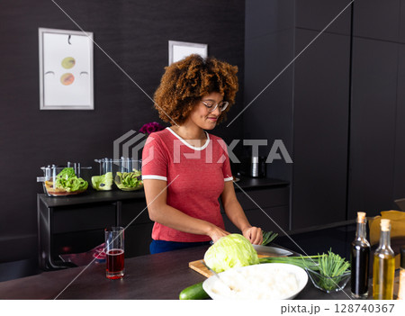 Diverse woman slicing cabbage on cutting board at modern kitchen island, with chopped vegetables Diverse woman slicing cabbage on cutting board at modern kitchen island, with chopped vegetables 128740367