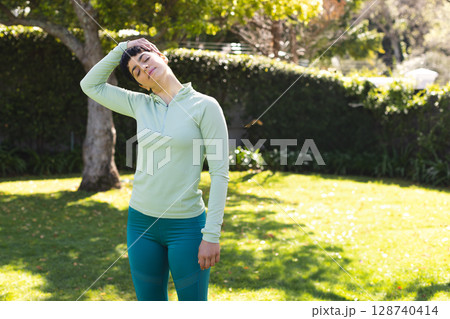 Young adult woman stretching neck on sunlit backyard lawn, enjoying tranquil morning exercise Young adult woman stretching neck on sunlit backyard lawn, enjoying tranquil morning exercise 128740414