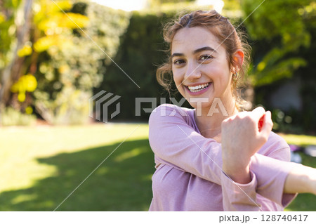 Woman stretching arm across chest in suburban backyard garden, enjoying sunny stretch, copy space Woman stretching arm across chest in suburban backyard garden, enjoying sunny stretch, copy space 128740417