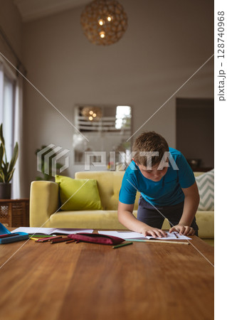 8-year-old boy drawing at coffee table in living room, with colored pencils and blue tablet cover 128740968