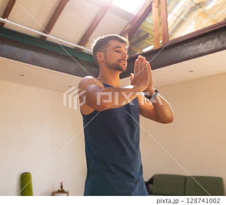 Young adult male practicing meditation in loft-style room with yoga mat and candle-lit side table 128741002