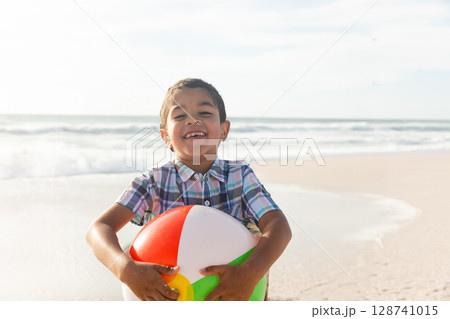Child boy holding colorful beach ball on sandy shoreline, with ocean waves rolling Child boy holding colorful beach ball on sandy shoreline, with ocean waves rolling 128741015