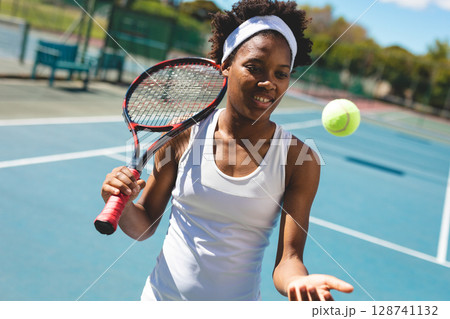 Female tennis player holding tennis racket, tossing tennis ball on outdoor court wearing headband Female tennis player holding tennis racket, tossing tennis ball on outdoor court wearing headband 128741132