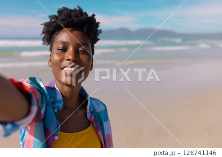 African American woman smiling and taking selfie on sunny sandy beach near ocean waves, copy space African American woman smiling and taking selfie on sunny sandy beach near ocean waves, copy space 128741146