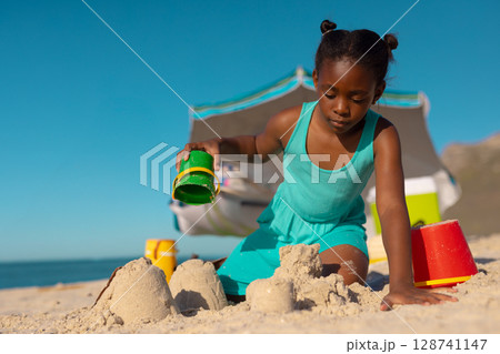 African American child kneeling on sand at beach building sandcastles with green bucket, copy space African American child kneeling on sand at beach building sandcastles with green bucket, copy space 128741147