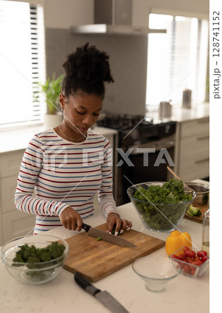 Woman chopping kale at kitchen island in home kitchen, with knife, bell pepper and cherry tomatoes Woman chopping kale at kitchen island in home kitchen, with knife, bell pepper and cherry tomatoes 128741152