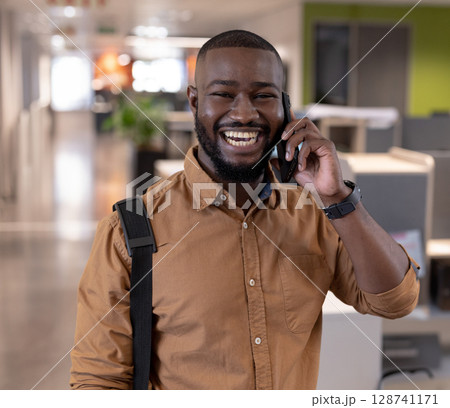 African American man talking on smartphone in modern office, with backpack strap and wristwatch 128741171