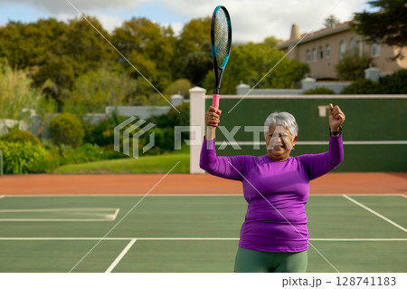Senior woman celebrating victory pumping fist and holding racket on home tennis court, copy space Senior woman celebrating victory pumping fist and holding racket on home tennis court, copy space 128741183