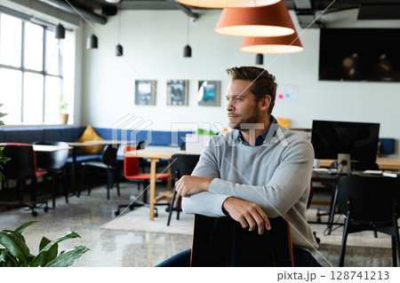 Man sitting on backward office chair in coworking space, with hanging lights, copy space Man sitting on backward office chair in coworking space, with hanging lights, copy space 128741213