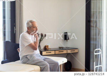 Senior man sitting on therapy table in therapy room holding painful neck with walker, copy space Senior man sitting on therapy table in therapy room holding painful neck with walker, copy space 128741214