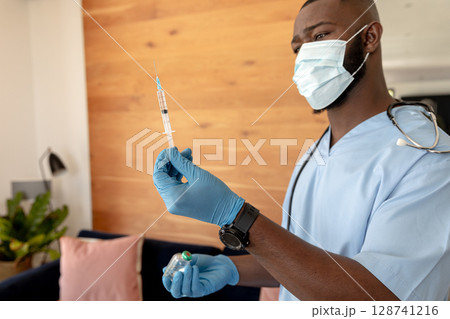 African American male clinician inspecting syringe and vial at clinic with stethoscope, copy space 128741216