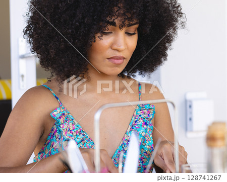 Young woman sitting at dining table indoors, examining utensils and metal frame with glass bottle Young woman sitting at dining table indoors, examining utensils and metal frame with glass bottle 128741267