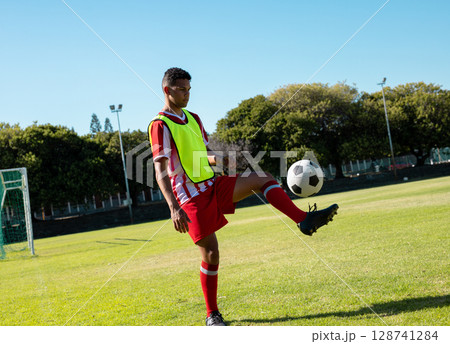 Male soccer player juggling soccer ball on soccer pitch, with fluorescent yellow bib, copy space Male soccer player juggling soccer ball on soccer pitch, with fluorescent yellow bib, copy space 128741284