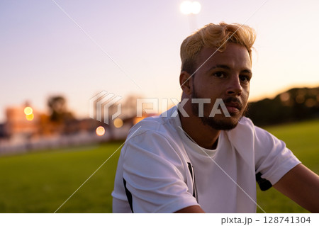 Man leaning on sports field edge at dusk, gazing toward stadium lights, copy space 128741304