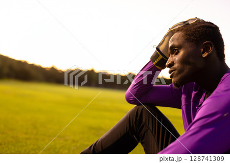 Teenage bi-racial boy sitting on field at golden hour, with glove and sunglasses, copy space 128741309