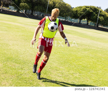 bi-racial male soccer player controlling ball mid-air on grass field, with neon-yellow bib bi-racial male soccer player controlling ball mid-air on grass field, with neon-yellow bib 128741341