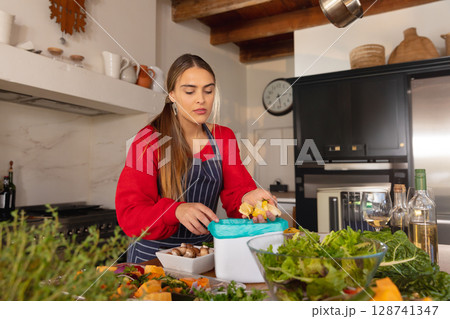 Woman prepping mushrooms on kitchen island in farmhouse kitchen, with vegetables and container 128741347