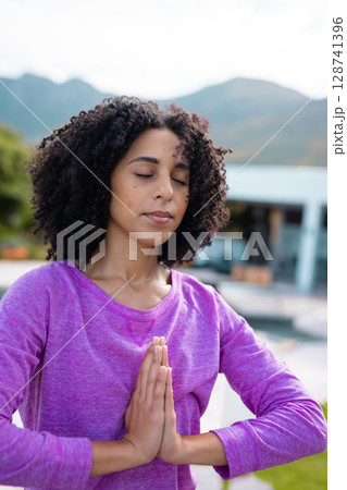Mid adult woman practicing yoga on poolside patio outside modern house, overlooking mountains Mid adult woman practicing yoga on poolside patio outside modern house, overlooking mountains 128741396