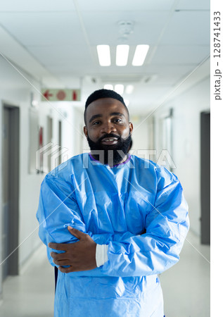 African American man standing in hospital corridor, wearing blue medical gown over scrubs 128741433