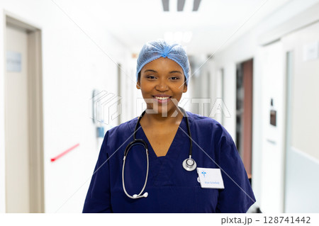 Female nurse smiling and standing in hospital corridor, wearing surgical cap, stethoscope, ID badge Female nurse smiling and standing in hospital corridor, wearing surgical cap, stethoscope, ID badge 128741442