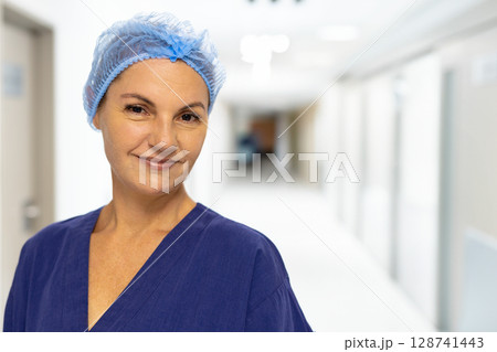 Female nurse standing and smiling in hospital corridor, wearing navy-blue scrub top and hairnet Female nurse standing and smiling in hospital corridor, wearing navy-blue scrub top and hairnet 128741443
