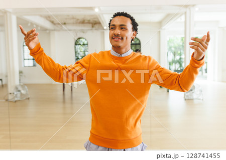 Man practicing dance moves in dance studio, using mirror panels and wooden ballet barre 128741455