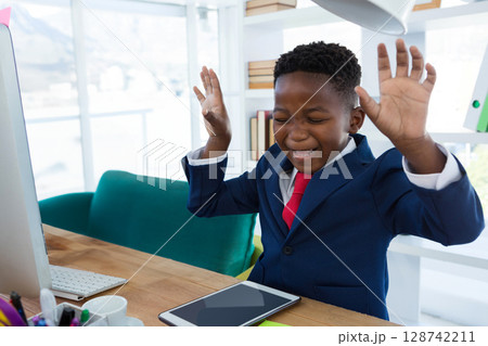 African American child raising both hands and smiling in home office, with tablet and monitor African American child raising both hands and smiling in home office, with tablet and monitor 128742211