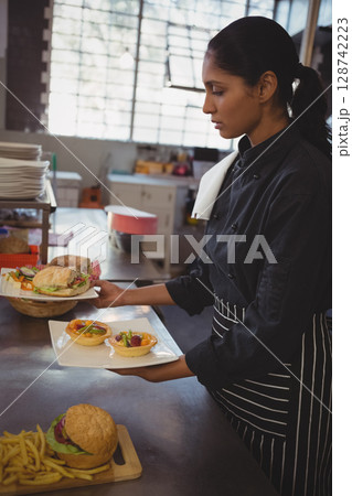 Indian woman chef plating tartlets and sandwiches on white plate in restaurant kitchen, copy space 128742223