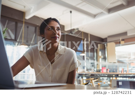 Indian woman working on open laptop at wooden table in modern café, showing focus, copy space 128742231