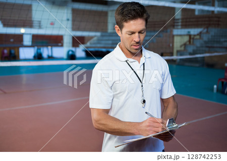 Mid adult man writing on clipboard in indoor volleyball court, with whistle and net, copy space Mid adult man writing on clipboard in indoor volleyball court, with whistle and net, copy space 128742253