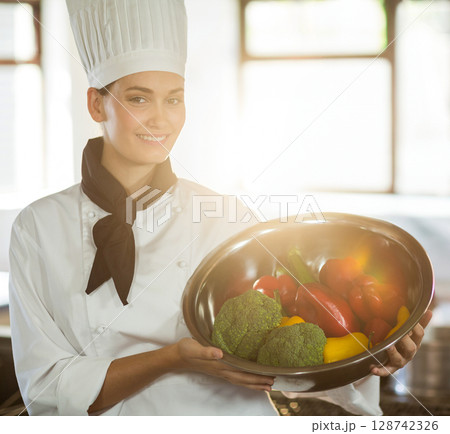 female chef wearing toque holding metal bowl with broccoli and peppers in restaurant kitchen female chef wearing toque holding metal bowl with broccoli and peppers in restaurant kitchen 128742326