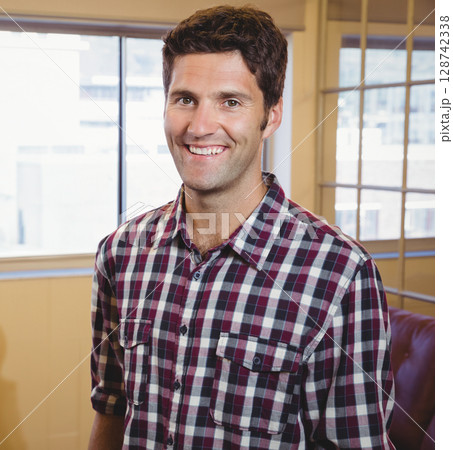 Man smiling while standing in office space by windows with wooden frames, leather chair, copy space 128742338