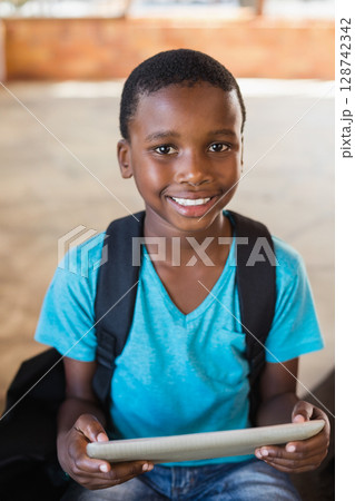 African American child holding tablet and carrying backpack in school hallway, smiling at camera African American child holding tablet and carrying backpack in school hallway, smiling at camera 128742342