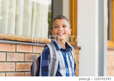 Young boy standing in front of brick building with window, wearing grey backpack and smiling face Young boy standing in front of brick building with window, wearing grey backpack and smiling face 128742343