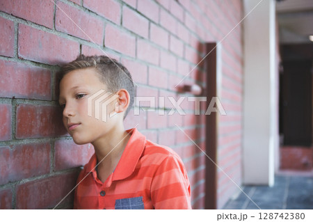 8-year-old boy leaning head on red brick wall in covered corridor with white columns, copy space 128742380