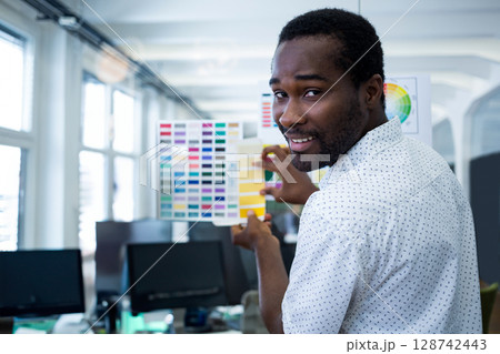 African American man holding up color swatch book in modern open office, exploring design options African American man holding up color swatch book in modern open office, exploring design options 128742443