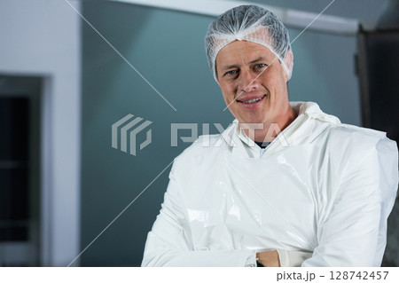 Man standing inside sterile cleanroom facility, wearing disposable hair net and protective coverall 128742457