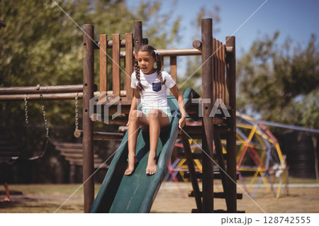 Girl child sliding down green plastic slide in park playground, enjoying sunny outdoor fun 128742555