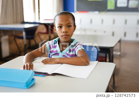 African American child studying at desk in elementary classroom, with open workbook and blue folder African American child studying at desk in elementary classroom, with open workbook and blue folder 128742573