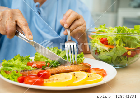 Asian elderly woman patient eating salmon stake and vegetable salad for healthy food in hospital. Asian elderly woman patient eating salmon stake and vegetable salad for healthy food in hospital. 128742831