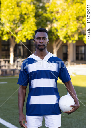 Mid-adult African American man standing on green sports field, with white sports ball 128742951