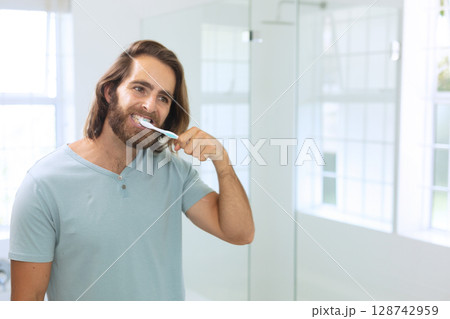 Young man brushing teeth in modern bathroom, with toothbrush and mirror, copy space 128742959