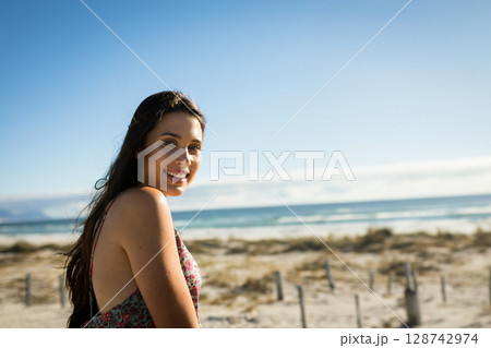 woman standing on sandy coastal dune, smiling over shoulder toward camera, copy space 128742974