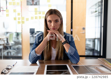 woman leaning forward at desk in modern office meeting room, using tablet and printed documents 128742985