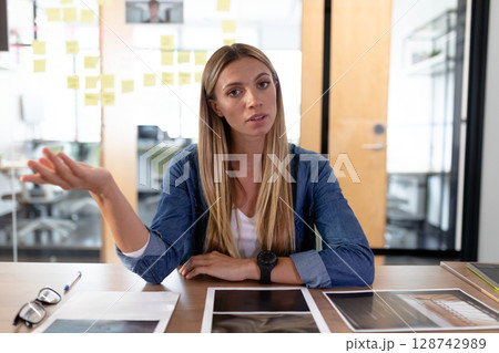 Woman sitting in modern office meeting room reviewing documents on tablet, with eyeglasses and pen 128742989