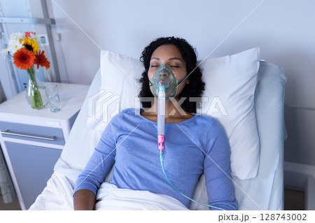 bi-racial young adult woman lying on hospital bed, wearing oxygen mask with flowers on table bi-racial young adult woman lying on hospital bed, wearing oxygen mask with flowers on table 128743002