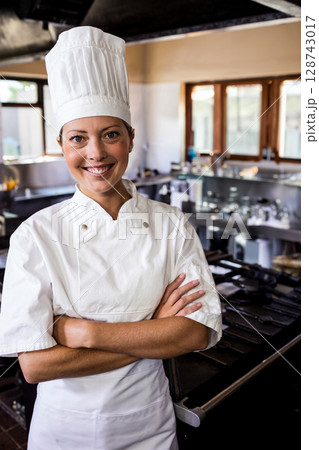 Female chef smiling and standing in restaurant kitchen, with chef's jacket, gas stove, copy space 128743017